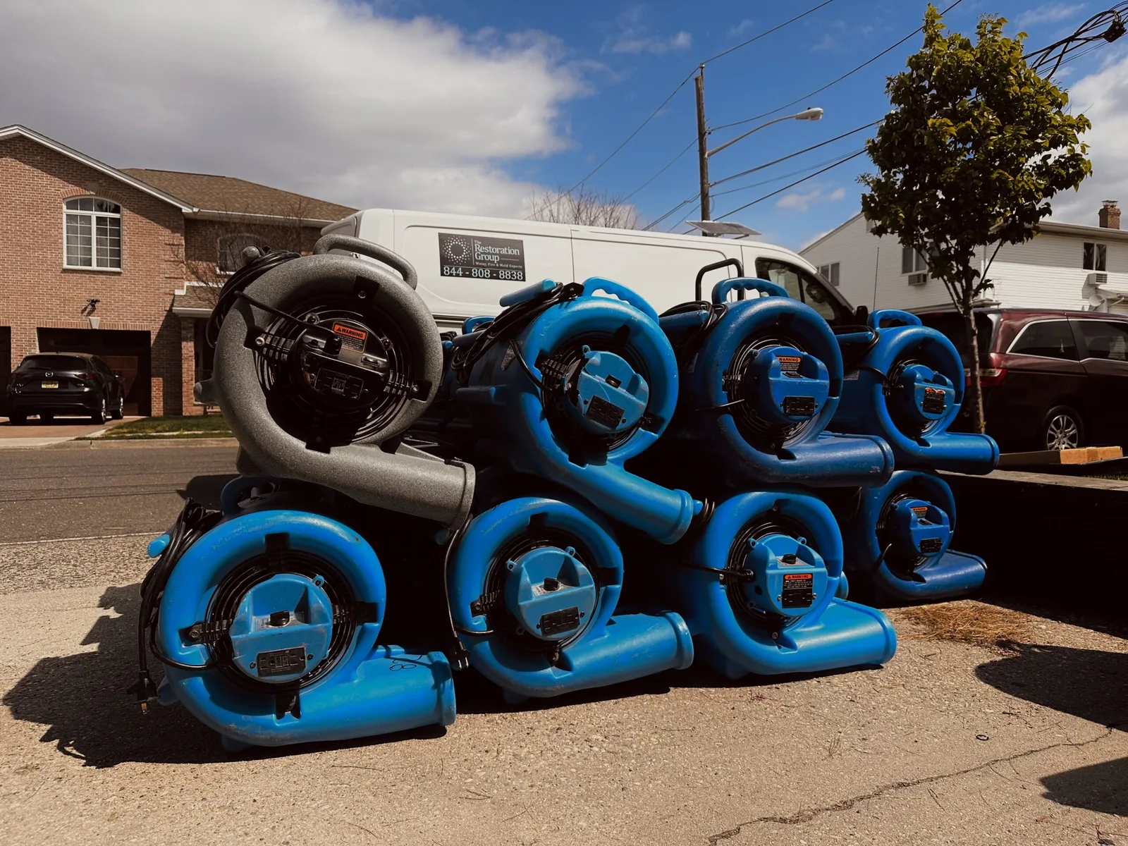 Air movers and drying equipment staged in front of a The Restoration Group van at a New Jersey job site