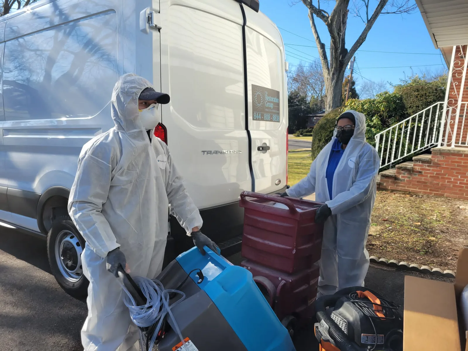 The Restoration Group technicians in protective suits unloading drying equipment from the company van